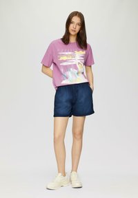 T-shirt graphique violet avec le design « Matin sous la mer », associé à un short bleu foncé et des baskets de couleur claire. Texture du tissu lisse.