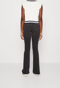 Černé rozšířené džíny se středně vysokým pasem, zadními kapsami a hladkou strukturou, doplněné o zkrácený bílý úpletový top senámo modrými pruhy.