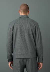 Chaqueta de pied de gallo gris con corte recto, cuello con muesca, puños abotonados y una textura suave. La vista trasera muestra detalles de sastrería.