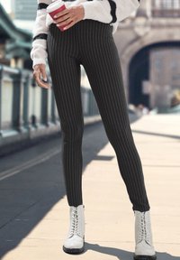 Zwarte gestreepte leggings met een hoge taille, gecombineerd met witte veterschoenen tot de enkel. Hand die een rode koffiekop vasthoudt. Gladde stofstructuur.