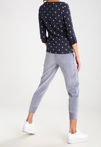 Haut bleu marine avec motif de cœurs blancs, manches trois-quarts ; joggings en velours gris ; baskets blanches ; coupe décontractée ; texture lisse ; tenue décontractée.