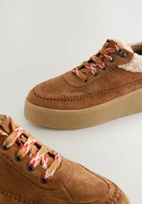 Brown suede sneakers with a textured upper, shearling lining, multicolored laces, and a light tan platform sole. Detailed stitching visible.