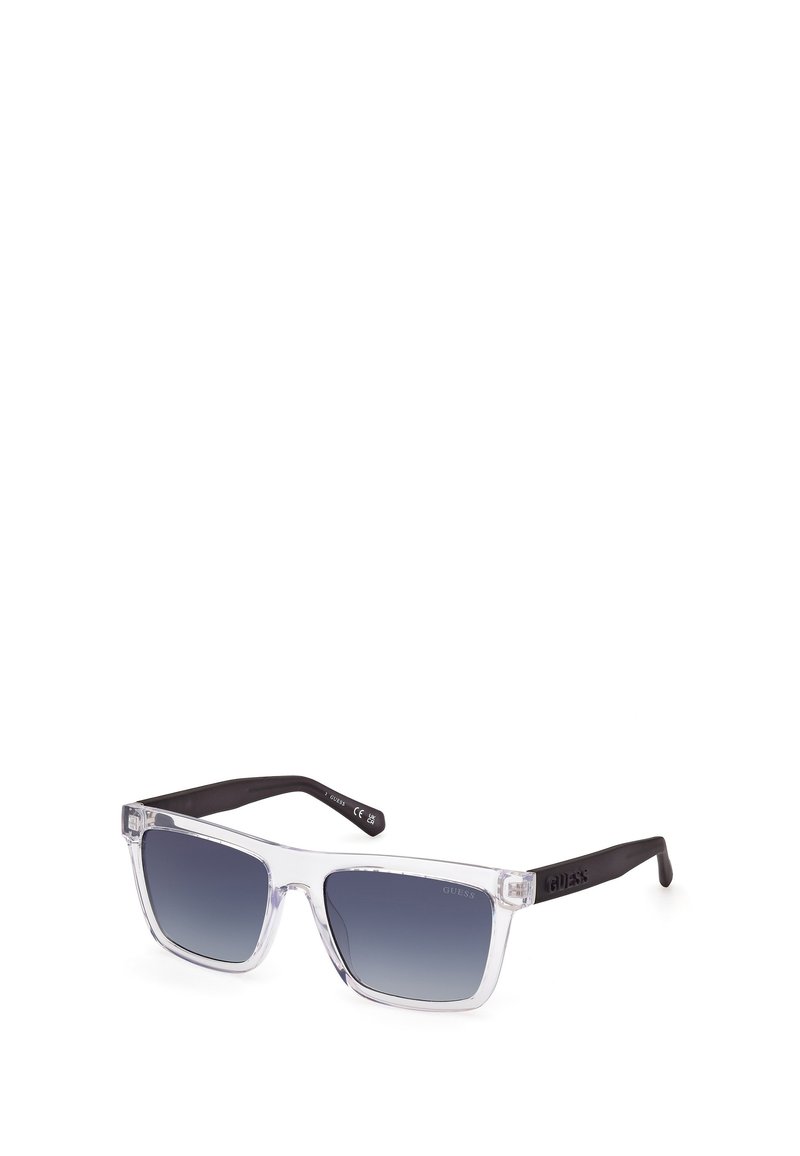 Gafas de sol de plástico transparente con lentes gris degradado y brazos negros. El diseño presenta una forma cuadrada y un sutil detalle del logo en la montura.