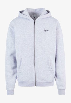 Sudadera con cremallera en gris claro, hecha de material suave. Presenta un corte relajado, dos bolsillos frontales y un logo bordado en el pecho.