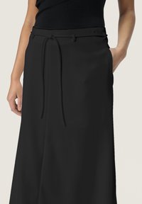 Zwarte wijde pantalons met een zachte textuur, voorzien van een trekkoord in de taille en zijzakken. De stof is lichtgewicht en vloeiend.