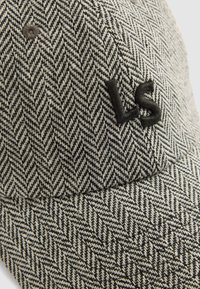 Gorra de patrón en espiga en blanco y negro con visera curva. Presenta un logo bordado "LS" en la parte frontal y una tela texturizada.