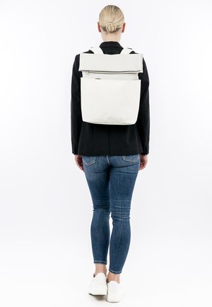 Mochila blanca con diseño de roll-top, hecha de material suave, con correas ajustables y un bolsillo frontal con cremallera. Apariencia limpia y moderna.
