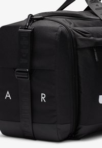 Sac en tissu noir de forme rectangulaire, doté d'une fermeture éclair, d'une bandoulière réglable et de détails en logo embossé sur la bandoulière et le corps.
