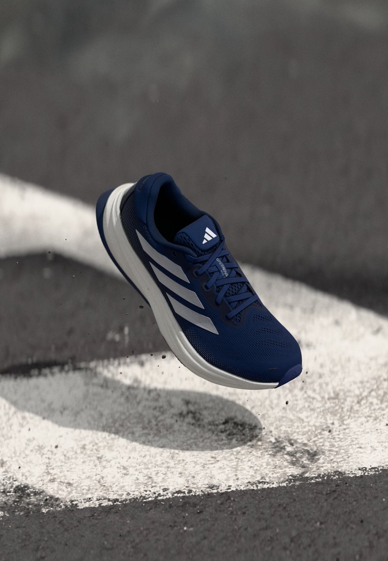 Blauer Sportschuh mit einem atmungsaktiven Mesh-Obermaterial, weißen Streifen und einer strukturierten Sohle. Leichtes und gepolstertes Design.