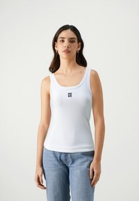 White tank top made from soft fabric, featuring a square neckline and small black "HUGO" logo on the chest. Paired with light blue jeans.