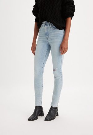 Jeans ajustados de color azul claro con detalles desgastados en las rodillas, hechos de mezclilla, combinados con botines negros y un suéter negro texturizado.