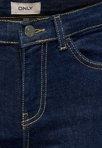 Temno modri džins hlače z zapiranjem na gumbom, rumenim šivom in oznako "ONLY" na pasu. Gladka tekstura in klasičen dizajn.