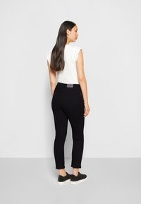 Jeans pretos ajustados com cintura alta, combinados com uma blusa branca de mangas curtas com bordas franzidas. Ténis pretos completam o visual.