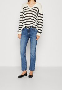 Randig stickad tröja i kräm och marinblått, vida ärmar, kombinerad med ljusblå jeans och svarta lägenheter. Har ett svart bälte med silverfäste.