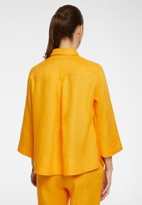 Yellow linen jacket with three-quarter sleeves, a collar, and a relaxed fit. Features side slits and a back seam detail.