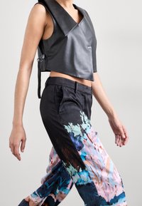 Haut court en cuir noir avec un grand col, associé à un pantalon léger à motifs dans des tons bleu, rose et noir. Texture lisse.