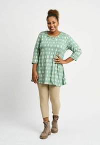 Tunic verde menta con motivi astratti bianchi, maniche a tre quarti, abbinata a leggings beige a capri e stivali lace-up color tan.