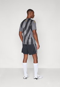 Grå sportsdrakt med svarte striper, svarte shorts og hvite knelange sokker; har en tettsittende design og en logo på skulderen.