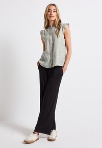 Blusa verde chiaro a righe con colletto alto e maniche a cappuccio, abbinata a pantaloni neri larghi e sneakers bianche con dettagli beige.
