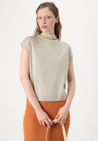 Lys beige ermeløs topp med høy hals og ribbestrikket kant, sammen med et oransje ribbestrikket skjørt. Enkel, jevn stofftekstur.