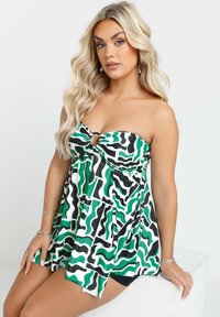 Vihreä ja musta kuviollinen olkaimeton toppi, jossa on keskellä pyöreä aukko. Valmistettu kevyestä kankaasta ja siinä on lentävä muotoilu.