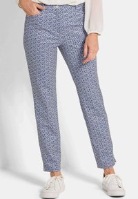 Blauwe pantalon met geometrisch patroon, gemaakt van lichte stof, gecombineerd met witte sneakers voor een casual look.