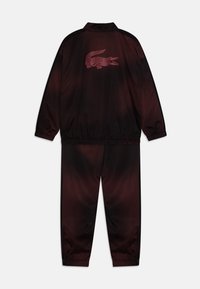 Survêtement rouge foncé avec un design dégradé. Comprend une taille élastique, des poignets élastiques et un logo crocodile en rose contrasté au dos.