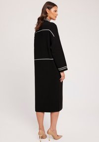 Czarna sukienka z długim rękawem, z białymi akcentami w przeszyciach, z ryżowym wzorem i prostym krojem. W komplecie z cielistymi szpilkami.