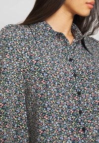 Floral button-up blouse in dark navy with a small-scale pattern of pink, blue, and green flowers; lightweight fabric and classic collar design.