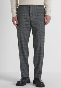 Grijs geruite broek van een wolmix met een ontspannen pasvorm, voorzien van subtiele blauwe accenten en een vlakke voorkant. Gecombineerd met zwarte laarzen met een dikke zool.