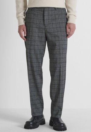 Grijs geruite broek van een wolmix met een ontspannen pasvorm, voorzien van subtiele blauwe accenten en een vlakke voorkant. Gecombineerd met zwarte laarzen met een dikke zool.