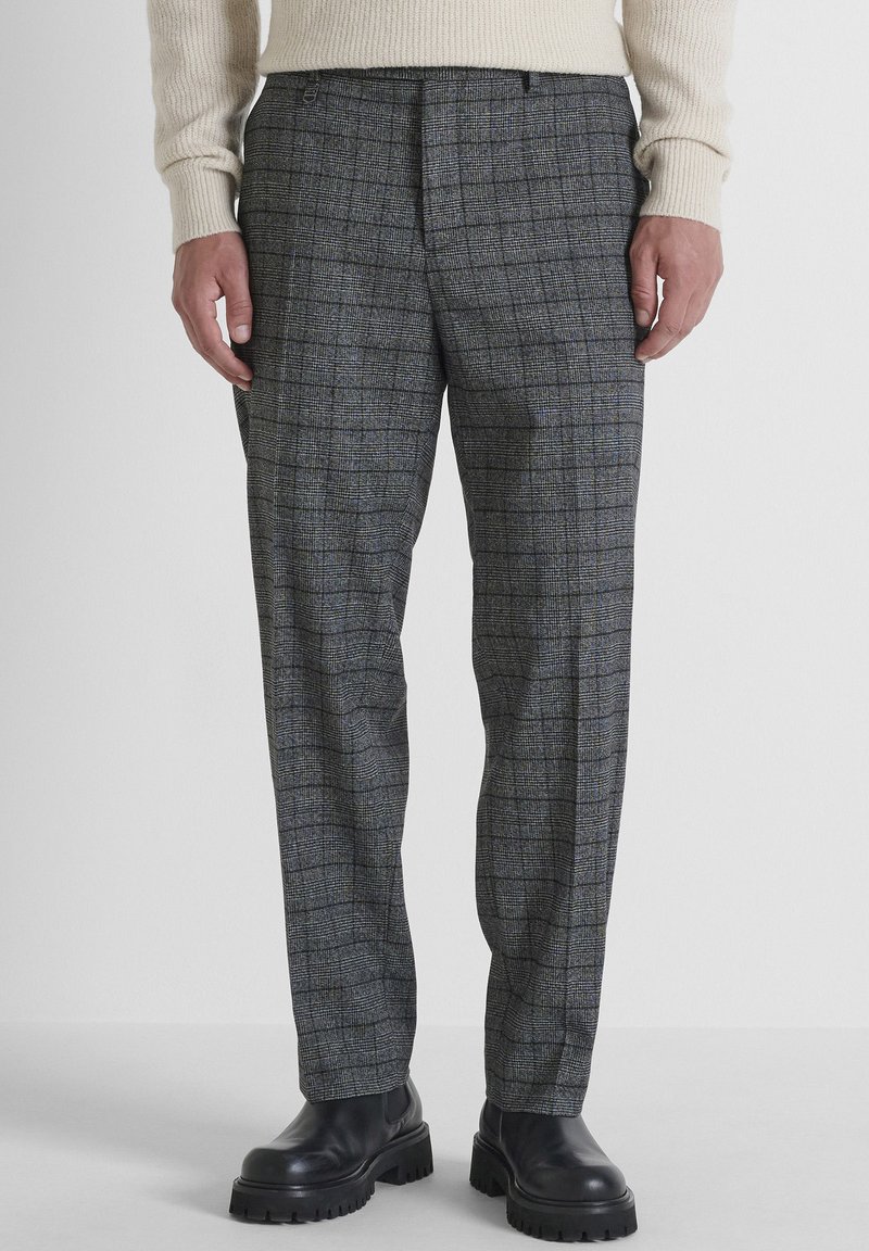 Grijs geruite broek van een wolmix met een ontspannen pasvorm, voorzien van subtiele blauwe accenten en een vlakke voorkant. Gecombineerd met zwarte laarzen met een dikke zool.