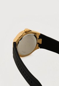 Cassa dell'orologio in acciaio inossidabile tonalità oro, con cassa rotonda in acciaio inox, cinturino in gomma nera e dettaglio testurizzato sul cinturino con corona a pressione.