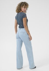 Blue jeans with a relaxed fit and flared legs, paired with a short-sleeve dark grey t-shirt. Smooth denim texture, subtle stitching.