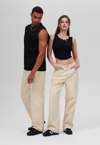 Black sleeveless top on a male and a black cropped top on a female, both wearing beige wide-leg pants and black sneakers.