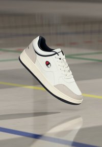 Λευκά αθλητικά παπούτσια με ανάγλυφη γκρι σουέντ επικάλυψη, μαύρες λεπτομέρειες και λογότυπο. Διαθέτουν παχύ, αντιθετικό πάτο και στρογγυλά κορδόνια.