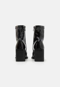 Bottes de cheville en cuir verni noir avec fermeture éclair, talons carrés et texture lisse. Pas de motifs visibles ni de détails matériels.