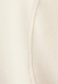 Tessuto a nido d'ape di colore bianco sporco con una cucitura visibile. Superficie morbida e leggermente testurizzata che conferisce un aspetto accogliente.