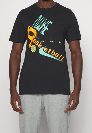 Camiseta negra con texto y logotipos abstractos y coloridos de "Nike Basketball", combinada con pantalones de chándal Nike de color gris claro.