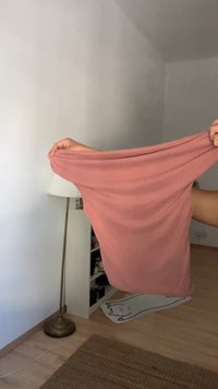 Svetloružová, elastická tkanina, ktorá sa drží, ukazuje svoju hladkú štruktúru a splývavosť. V pozadí je lampa a čiastočne viditeľná polica.