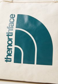 Platnena torba u off-white boji s tirkiznim kružnim grafičkim uzorkom i ispisanim tekstom "thenorthface" u podebljanom tipografskom stilu.