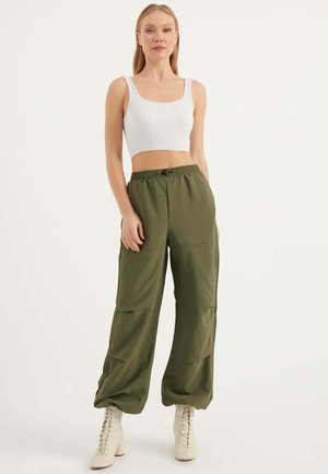 Pantalon large vert avec taille élastique et poches latérales, associé à un crop top ajusté blanc à côtes et des bottines beiges à lacets.