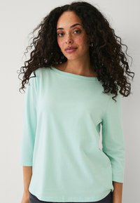 Camicia verde menta chiaro a maniche lunghe con scollatura larga e maniche a tre quarti, realizzata in un tessuto morbido e liscio.