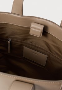 Beige læder tote taske med glat tekstur, åbent top og en lynlåslomme indeni. Har et mærketag og syede detaljer.