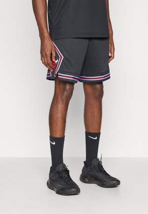 Shorts de sport noirs avec un ourlet rayé rouge et bleu et un logo. Assortis à des chaussures noires et des chaussettes Nike noires montantes.