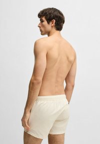 Light beige shorts made of textured fabric with an elastic waistband and a single back pocket, shown from a side and back view.