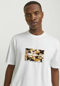 Hvid bomulds t-shirt med et centralt grafisk motiv i beige, sort og gul samt teksten "Original Studio", og en afslappet pasform.