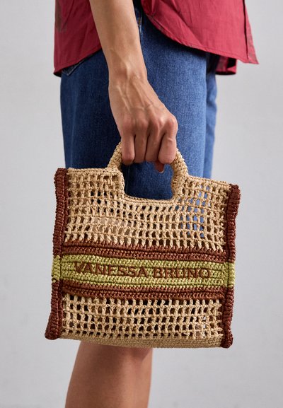 Sac en paille tissé avec des rayures beiges, vertes et brunes, doté de poignées renforcées et du texte "VANESSA BRUNO" sur le devant.