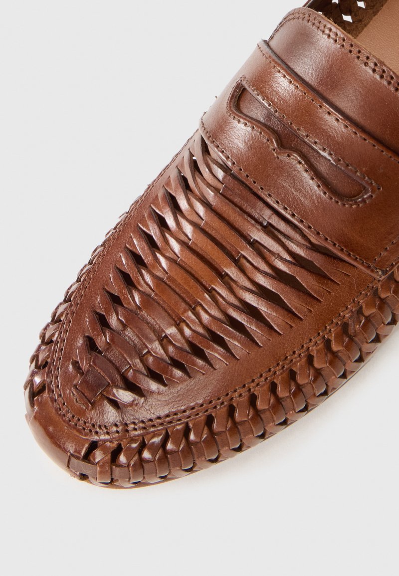 Brown leather shoe with woven design and stitched accents, featuring a rounded toe and textured surface.