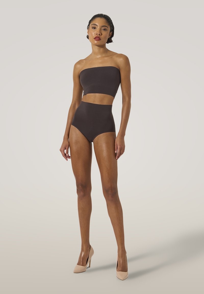 Brun tvådelad baddräkt med en strapless topp och hög midja, tillverkad av ett slätt material. Modell som står i nude högklackat.